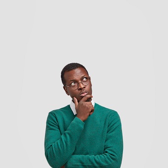 Indoor shot of contemplative dark skinned young man holds chin, looks thoughtfully upwards, dreams about something, thinks about future, dressed in green jumper, isolated over white background